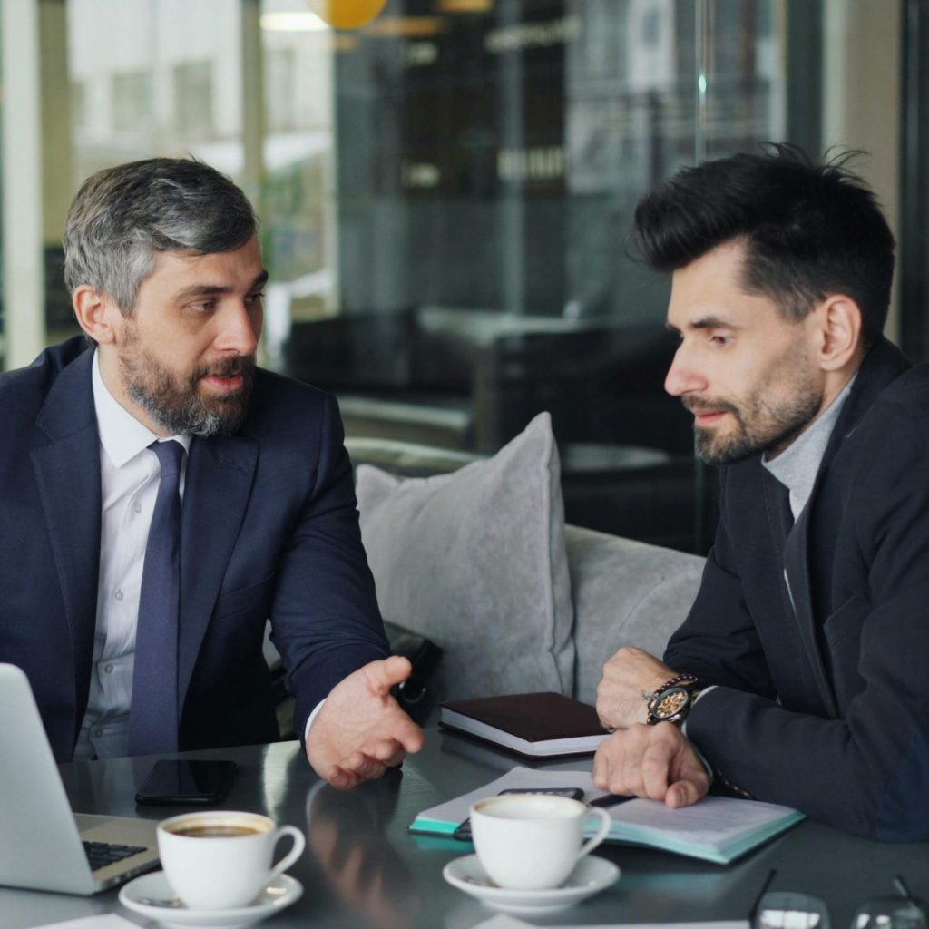 Two businessmen in a café having a professional discussion with coffee and a laptop.